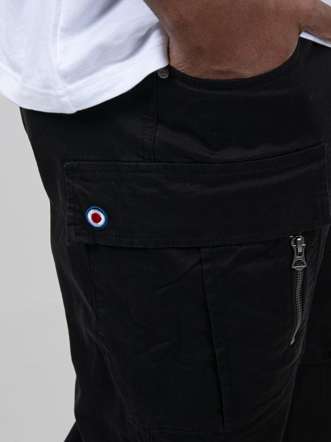 Close-up of Ben Sherman black cargo pants pocket with signature target logo badge and zip