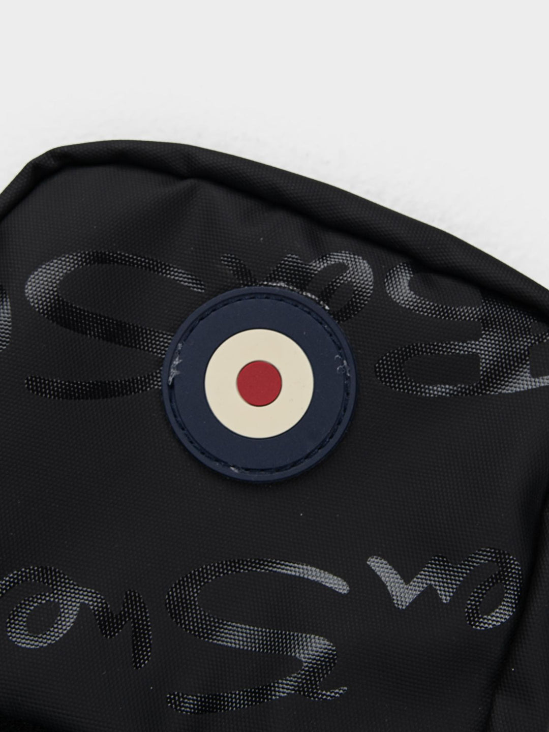 Close-up of Ben Sherman Compact Crossbody Bag in Black showing Mod target emblem badge and wax plastisol branding detail