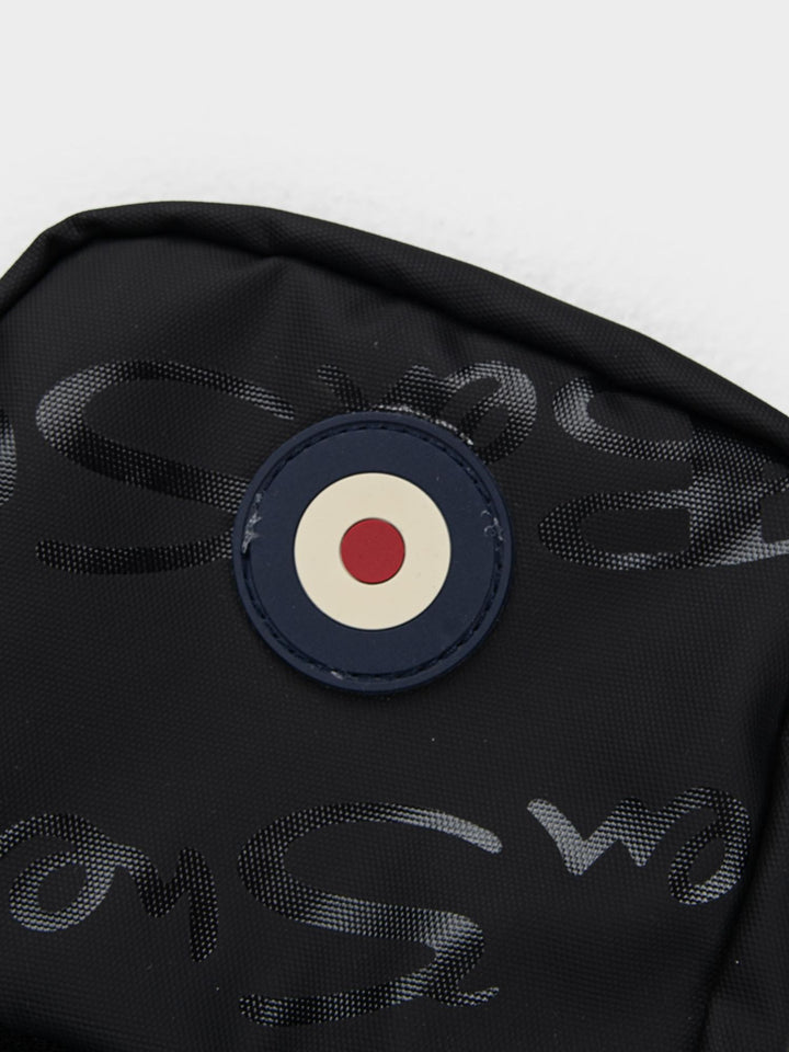 Close-up of Ben Sherman Compact Crossbody Bag in Black showing Mod target emblem badge and wax plastisol branding detail