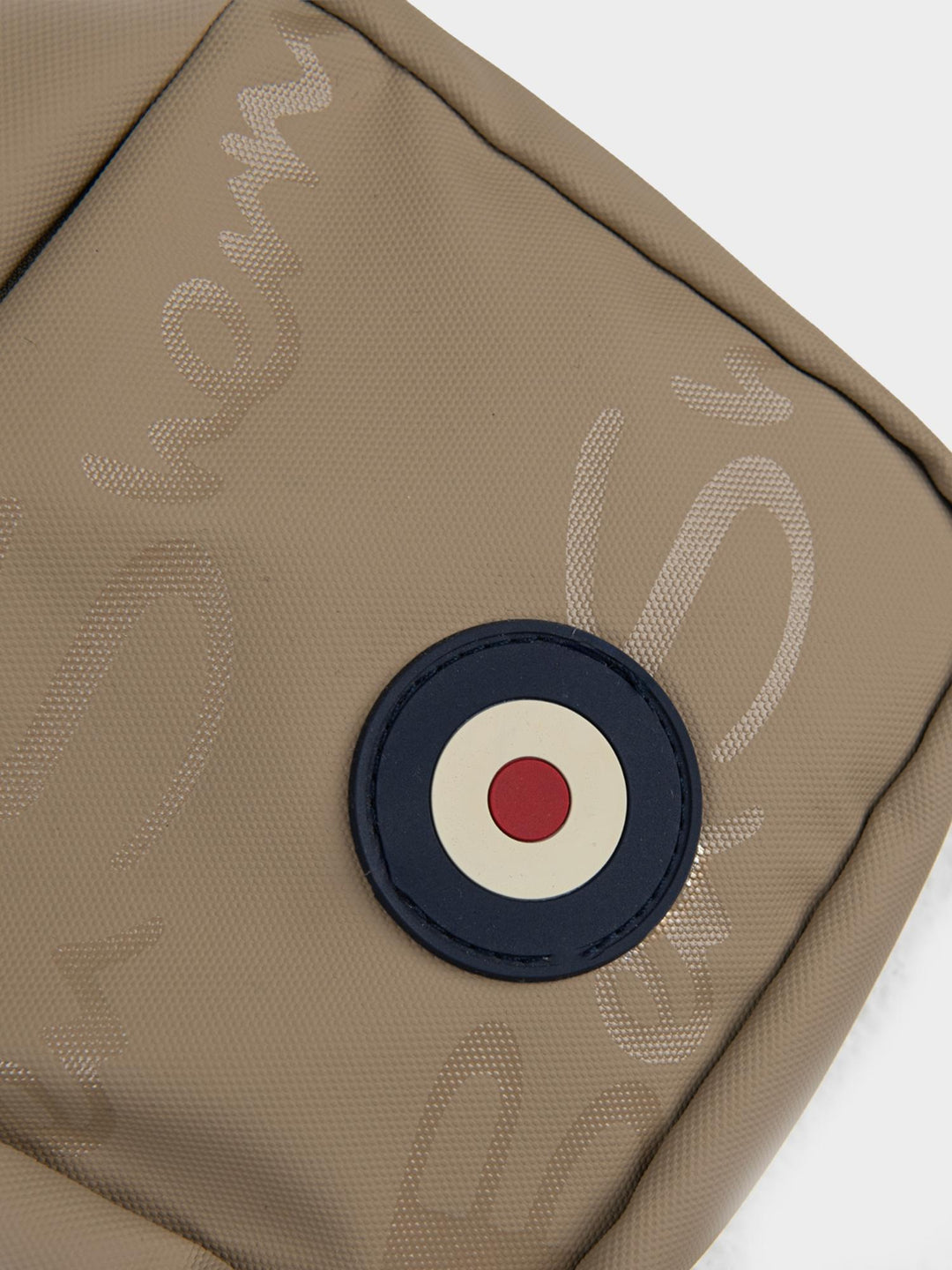 Close-up of Ben Sherman Compact Crossbody Bag in Stone showing Mod target emblem badge and wax plastisol branding detail