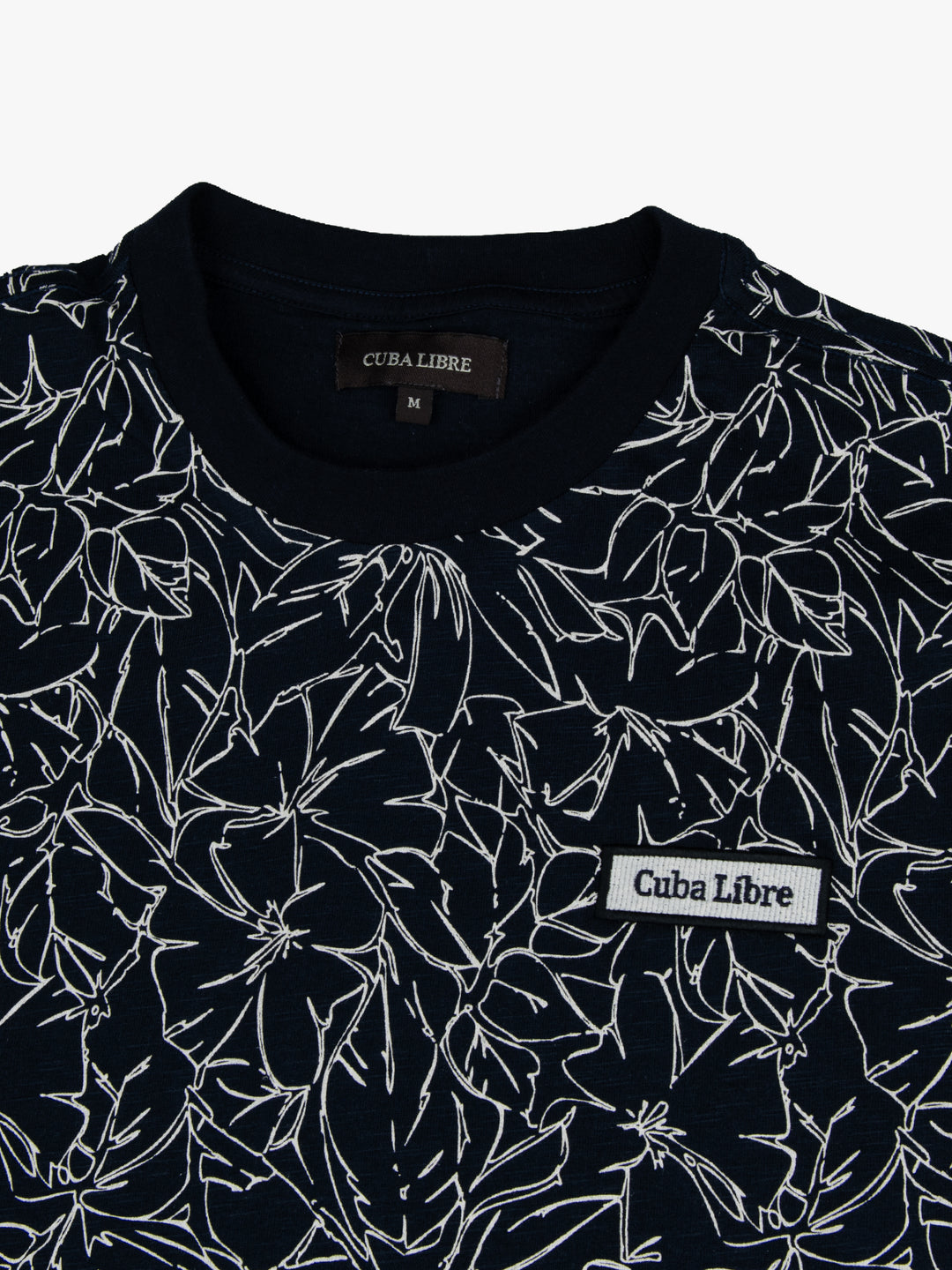 Close-up of Cuba Libre Tee in Captain Blue showing all-over floral print detail and woven logo patch at chest