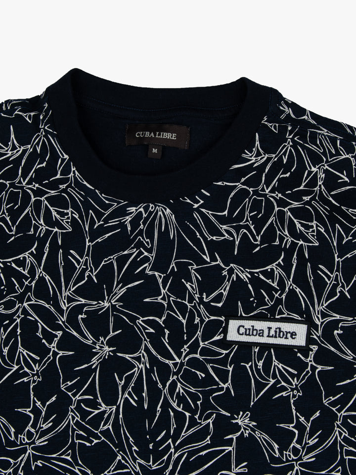 Close-up of Cuba Libre Tee in Captain Blue showing all-over floral print detail and woven logo patch at chest