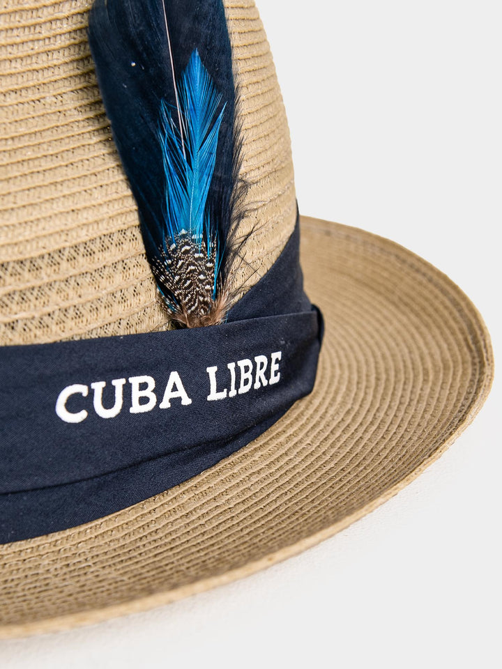 Close-up of Cuba Libre Fedora Straw Hat Beige - navy band with embroidered Cuba Libre logo and blue feather trim detail