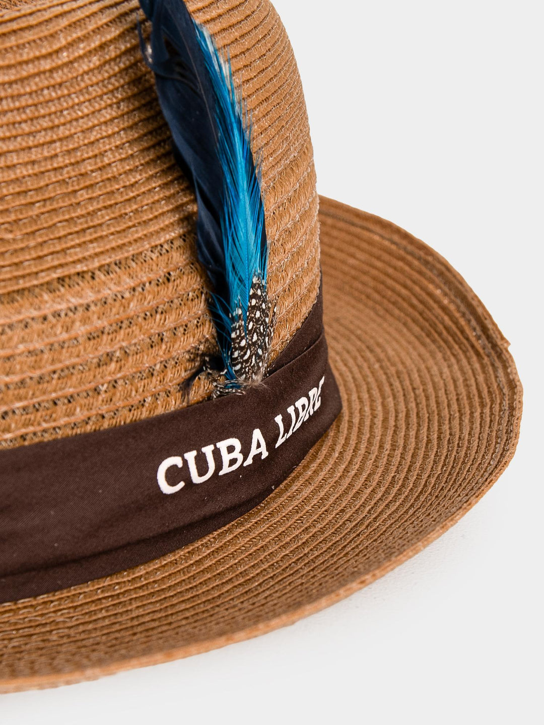 Close-up of Cuba Libre Fedora Straw Hat Gold - dark band with embroidered Cuba Libre logo and blue feather trim