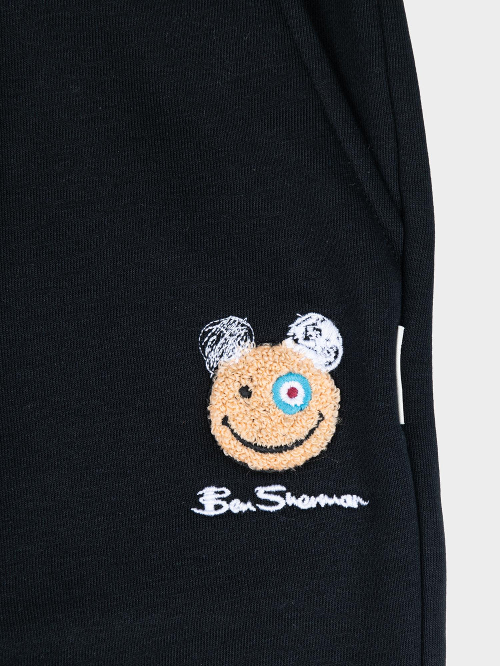 Close-up of embroidered Happy Bear motif and Ben Sherman logo on black fleece jog shorts