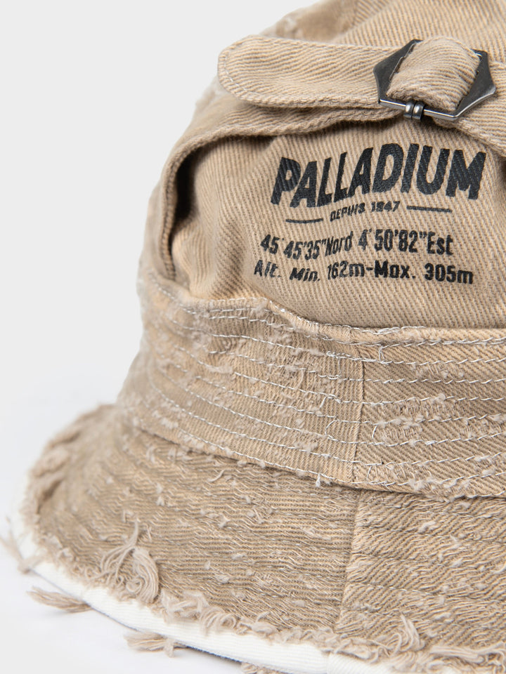Close-up of the stone Palladium frayed bucket hat showing the printed Palladium logo, buckle detail and frayed brim