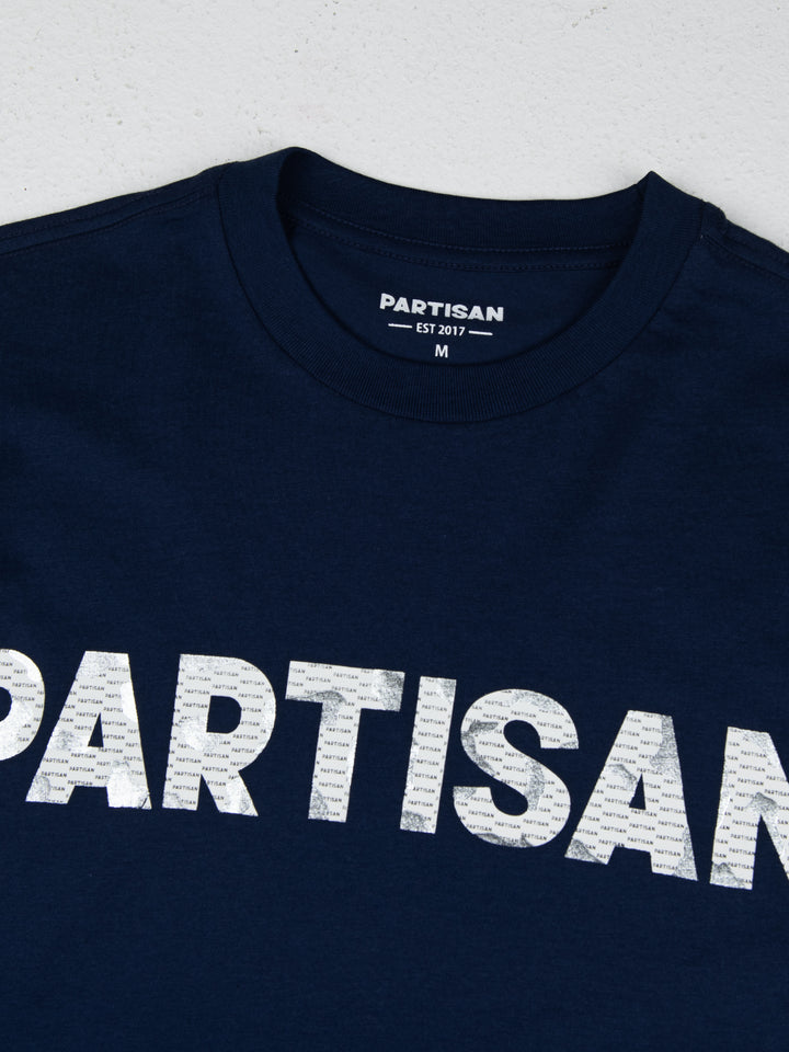 Close-up of Partisan foil print detail on Navy T-shirt — metallic PARTISAN logo text on deep navy fabric with woven neck label