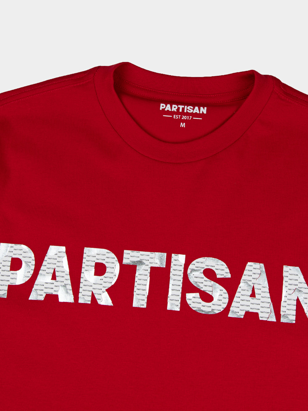 Close-up of Partisan foil print detail on red T-shirt — metallic PARTISAN logo text with woven neck label