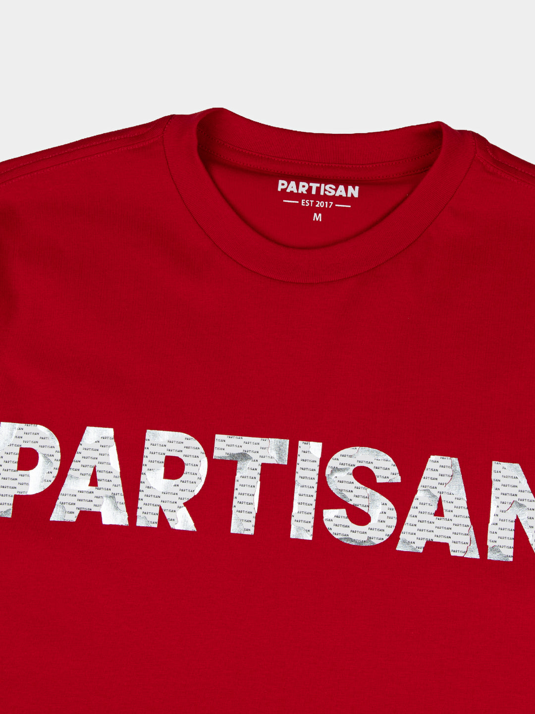Close-up of Partisan foil print detail on red T-shirt — metallic PARTISAN logo text with woven neck label