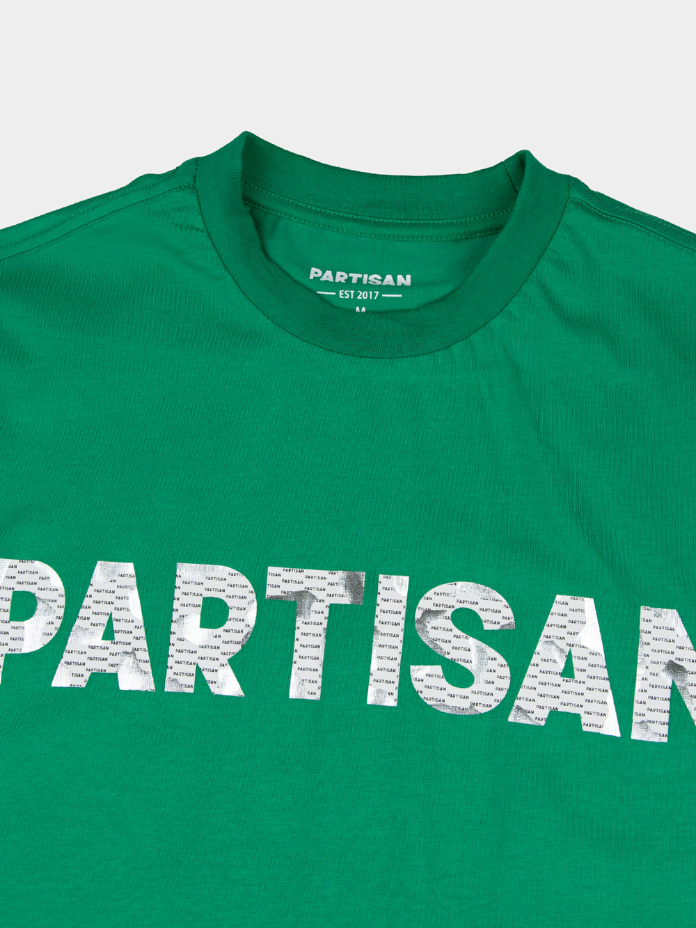Close-up of Partisan foil print detail on Staford Green T-shirt — metallic PARTISAN logo text on vivid green fabric with woven neck label