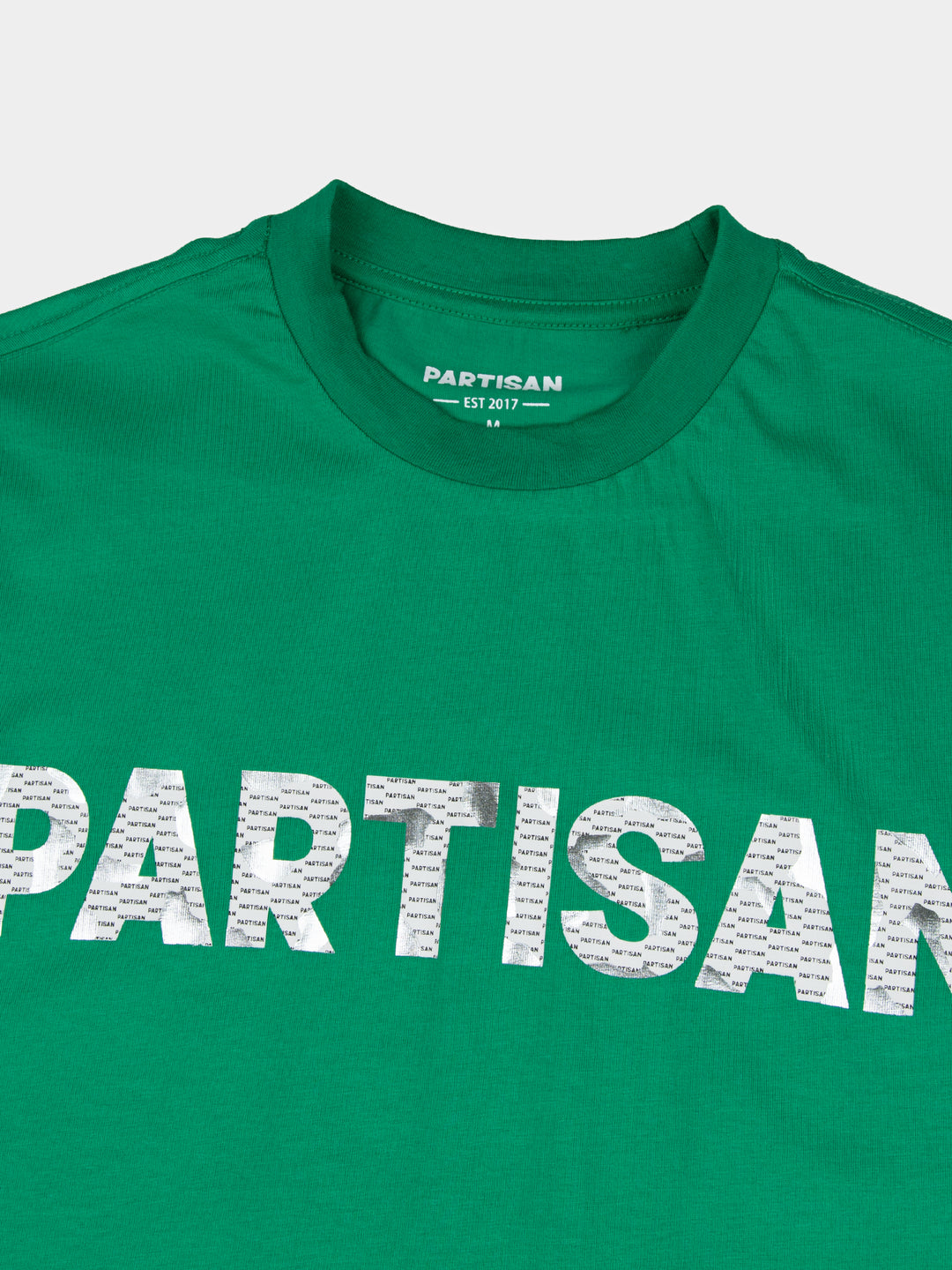 Close-up of Partisan foil print detail on Staford Green T-shirt — metallic PARTISAN logo text on vivid green fabric with woven neck label