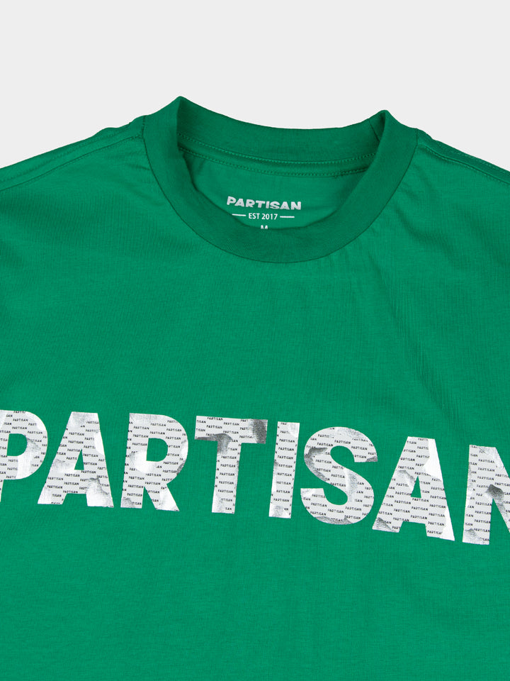 Close-up of Partisan foil print detail on Staford Green T-shirt — metallic PARTISAN logo text on vivid green fabric with woven neck label