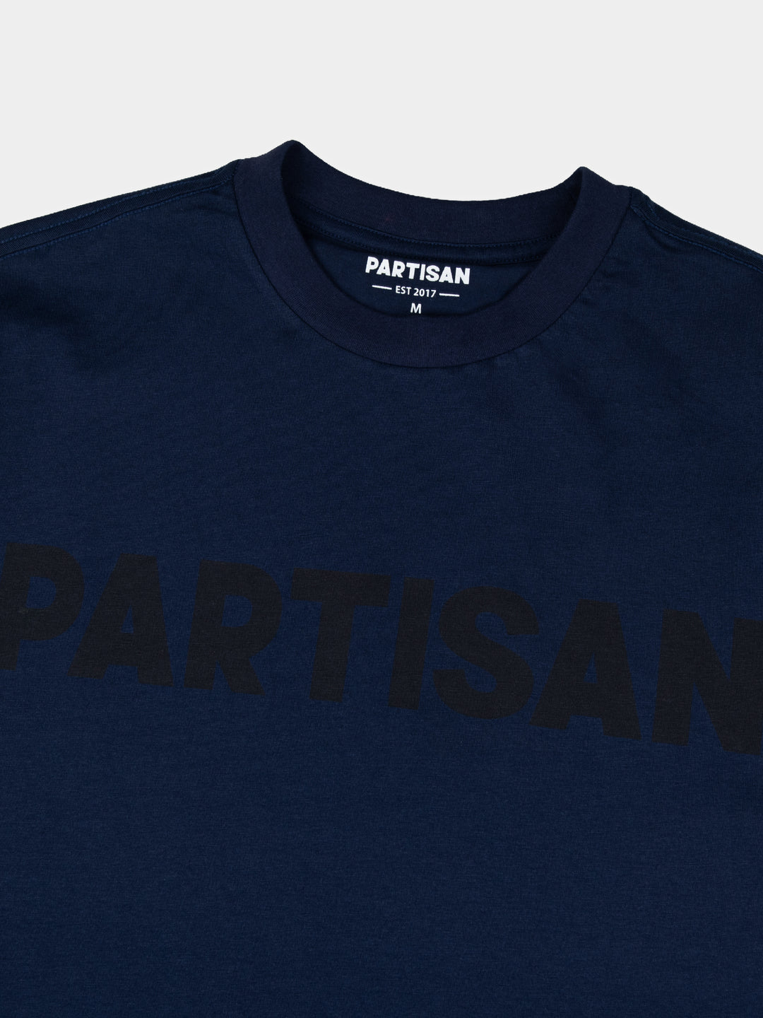 Partisan Tonal Print Tee in Navy – Close-up of tonal chest logo print and neck label on navy blue cotton t-shirt