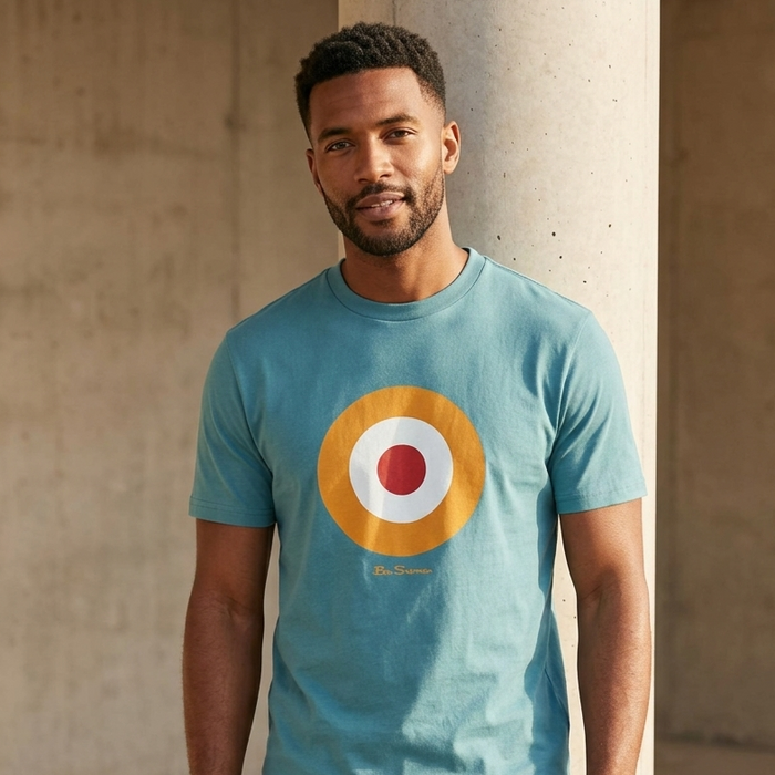 Man wearing a blue t-shirt with a colorful circular design against a concrete wall.